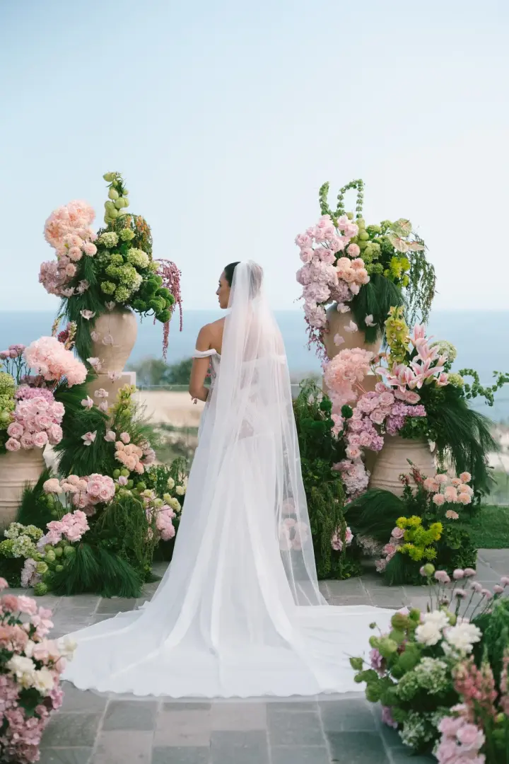 A bride in her veil facing the ocean before the ceremony