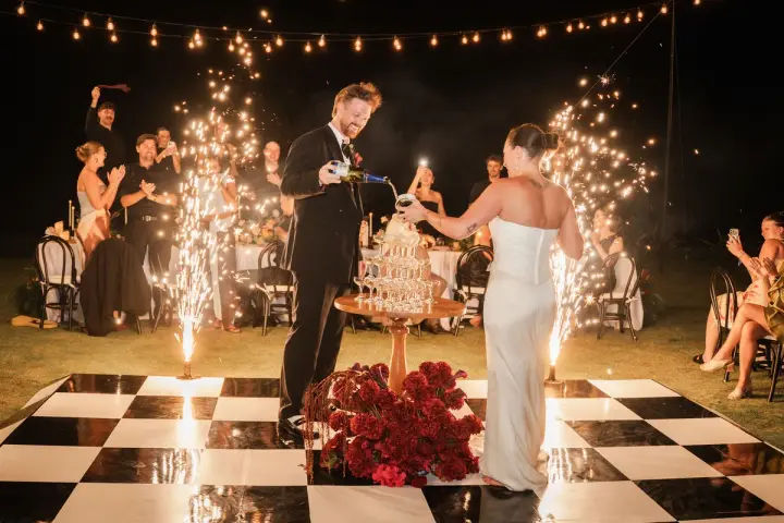 A couple cutting their cake on a checkered dance floor surrounded by rising sparklers