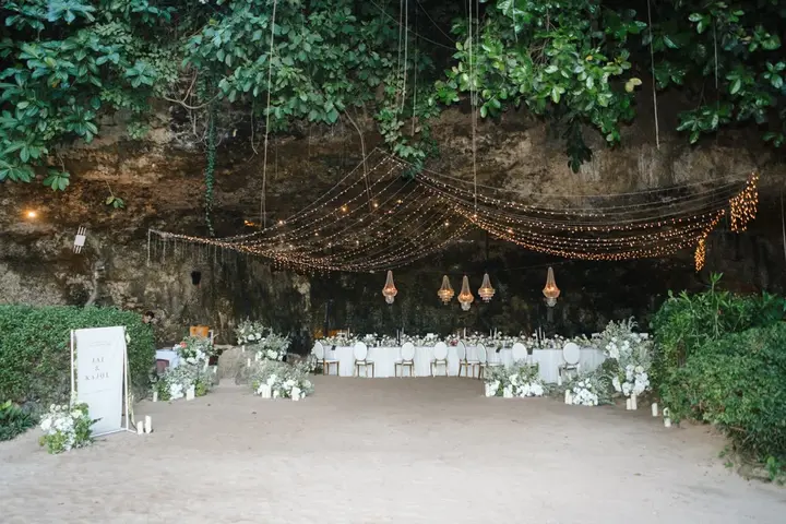 Long dining tables beneath festoon lights strung across a planted rock overhang
