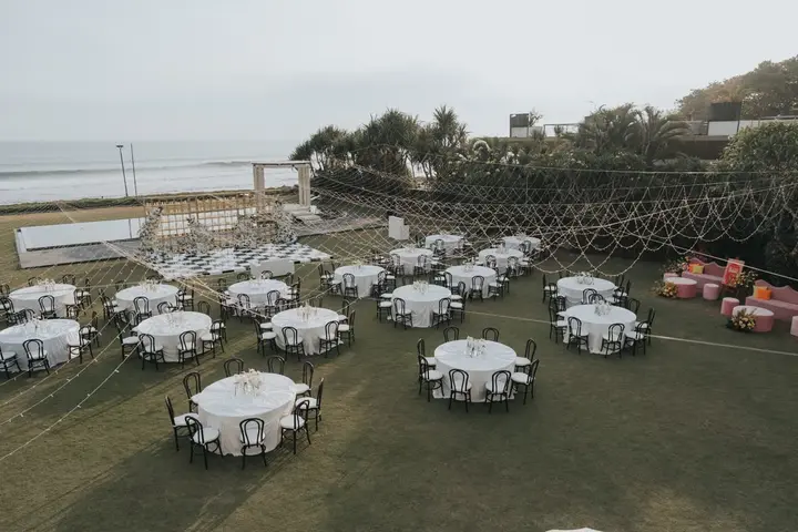 An aerial view of round reception tables set across a lawn beside the sea