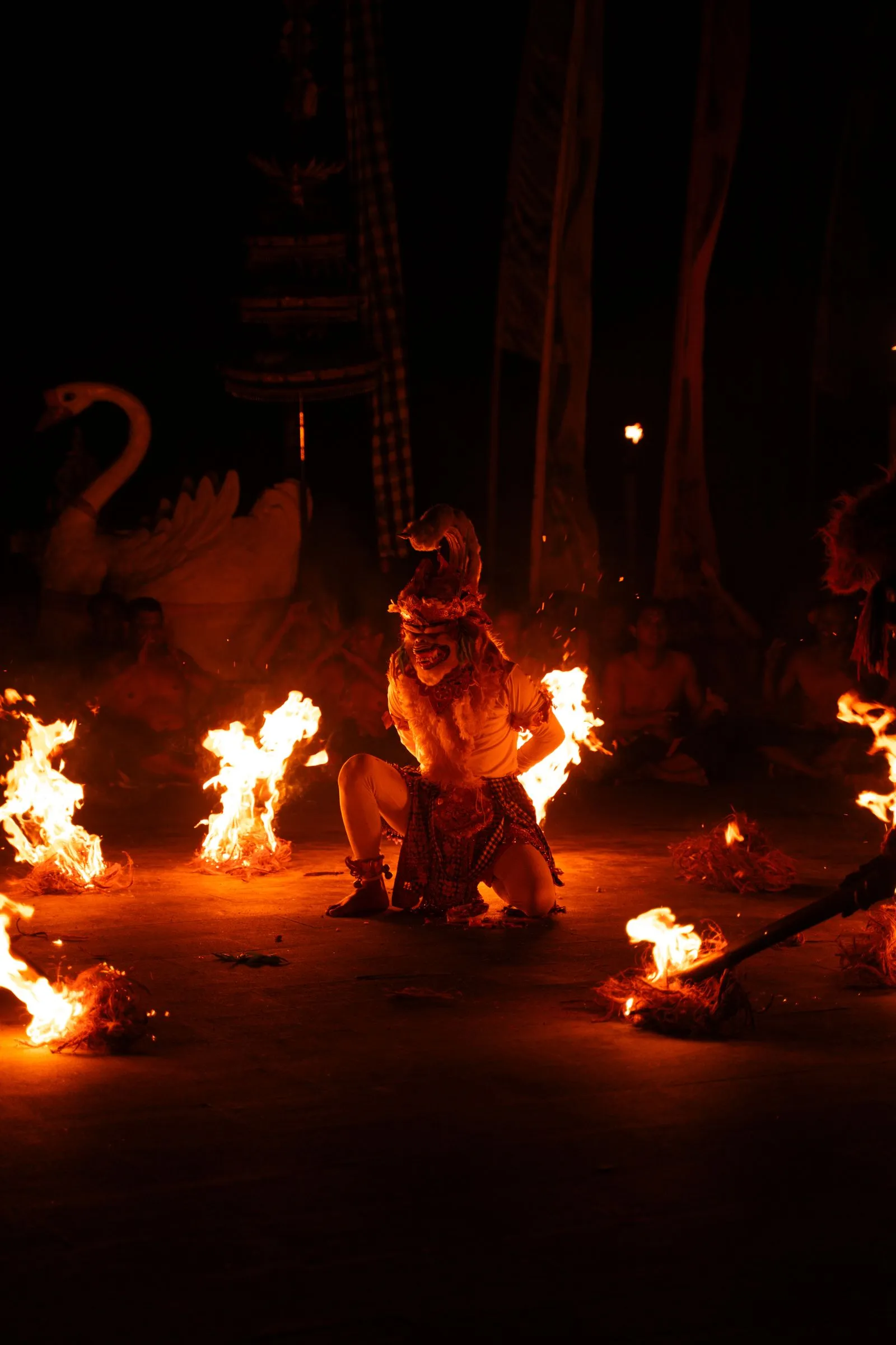 A traditional Balinese fire dancer mid-performance at night, surrounded by flames