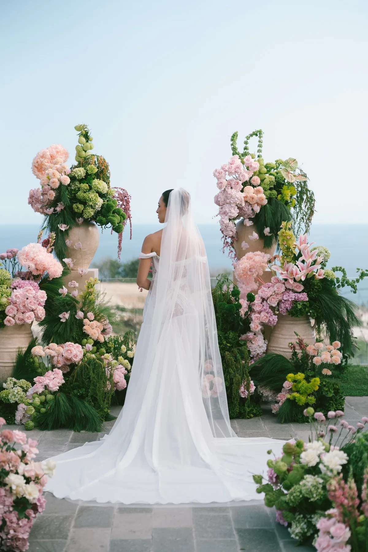 A bride in her veil, facing the ocean before the ceremony