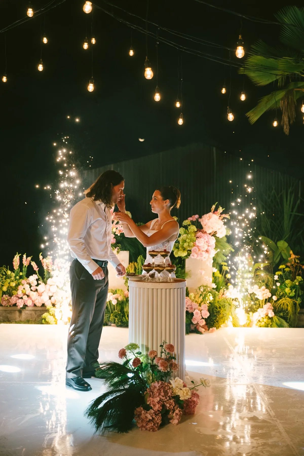 Isaac and Whitney at the cake, framed by sparklers and string lights