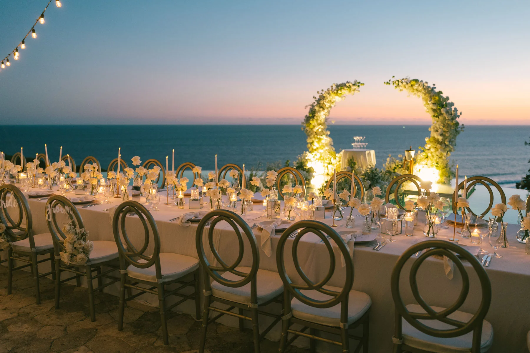 Oceanfront reception table at sunset beneath a moon arch