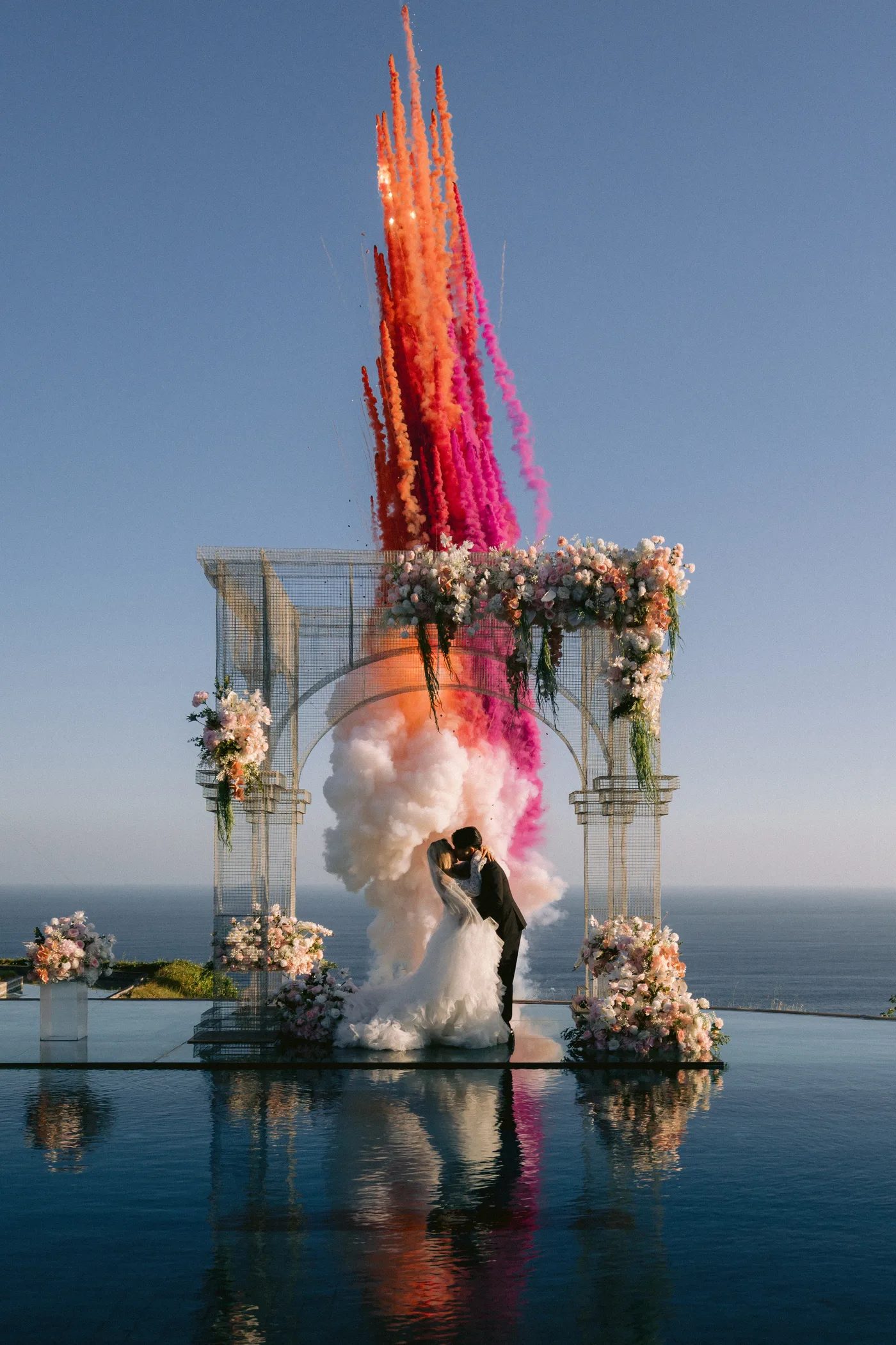 Coloured smoke rises above the ceremony arch as the couple kiss