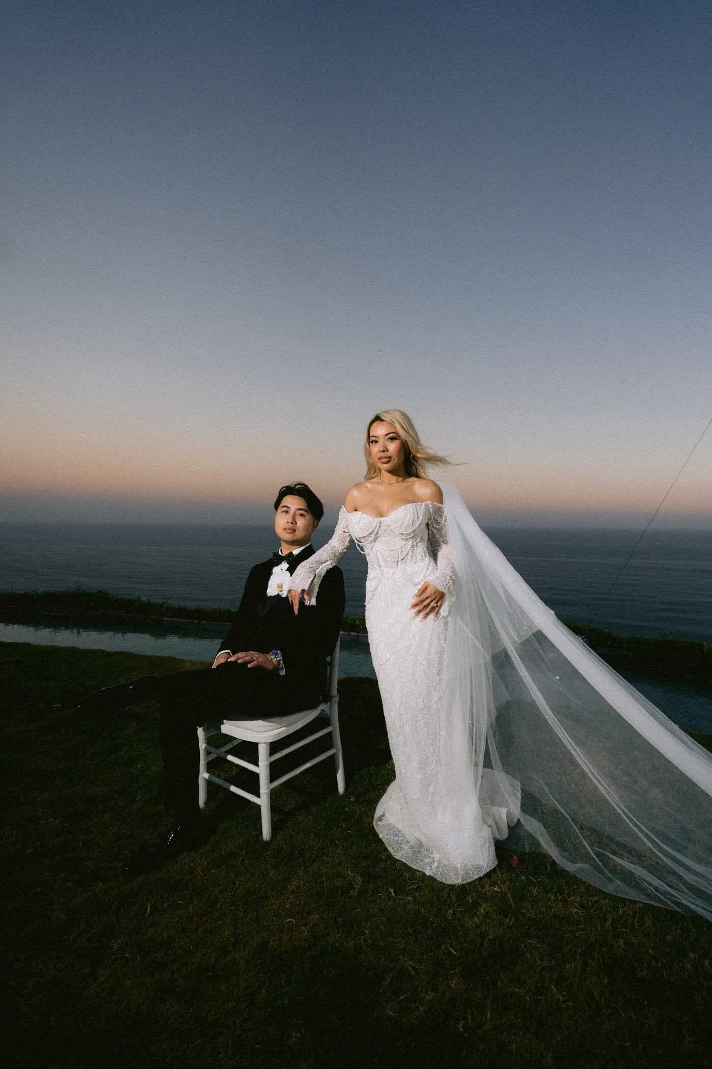 The newlyweds at dusk, veil catching the wind above the water
