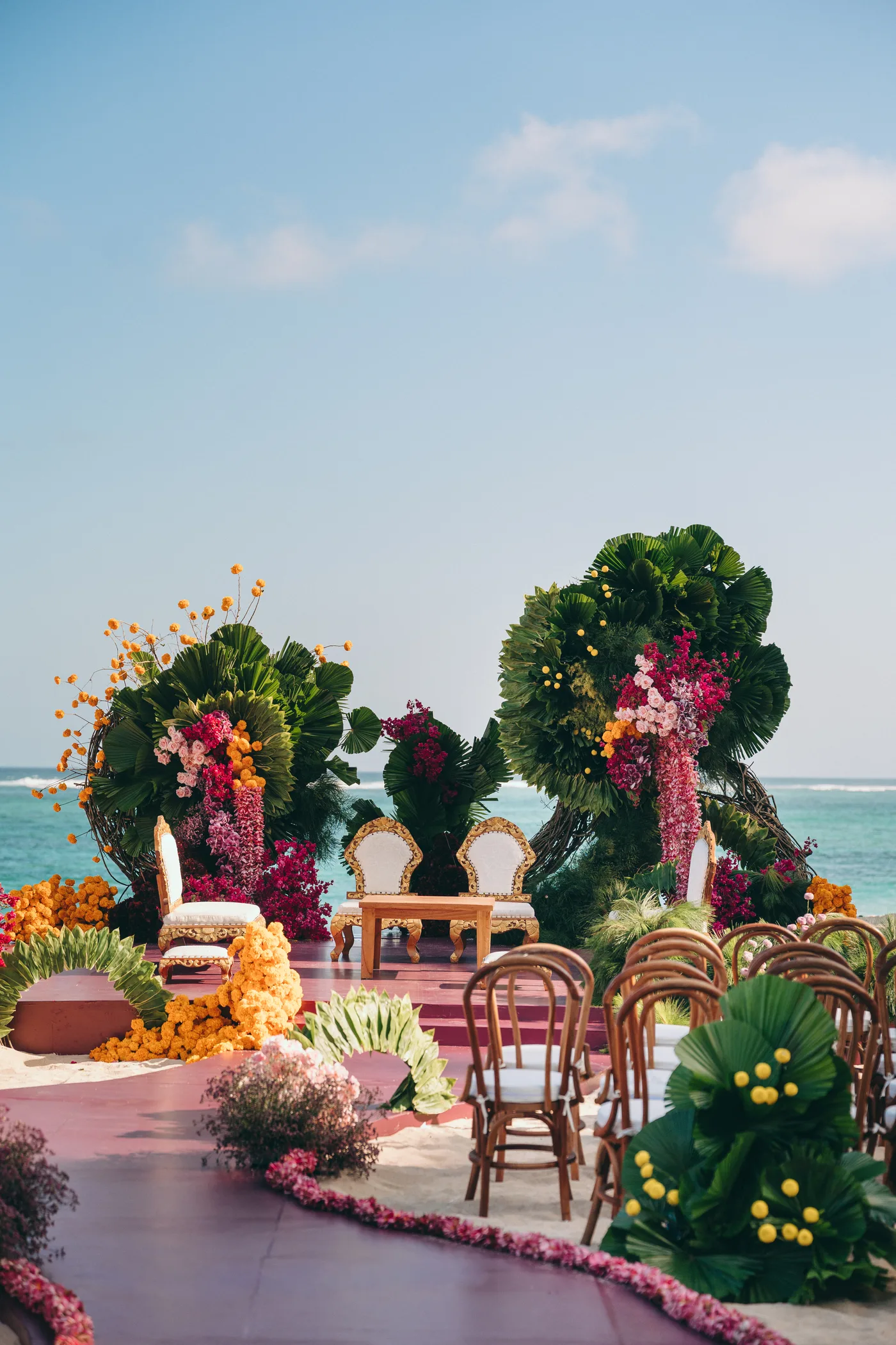 An oceanfront mandap ceremony stage with palm frond arches and marigolds