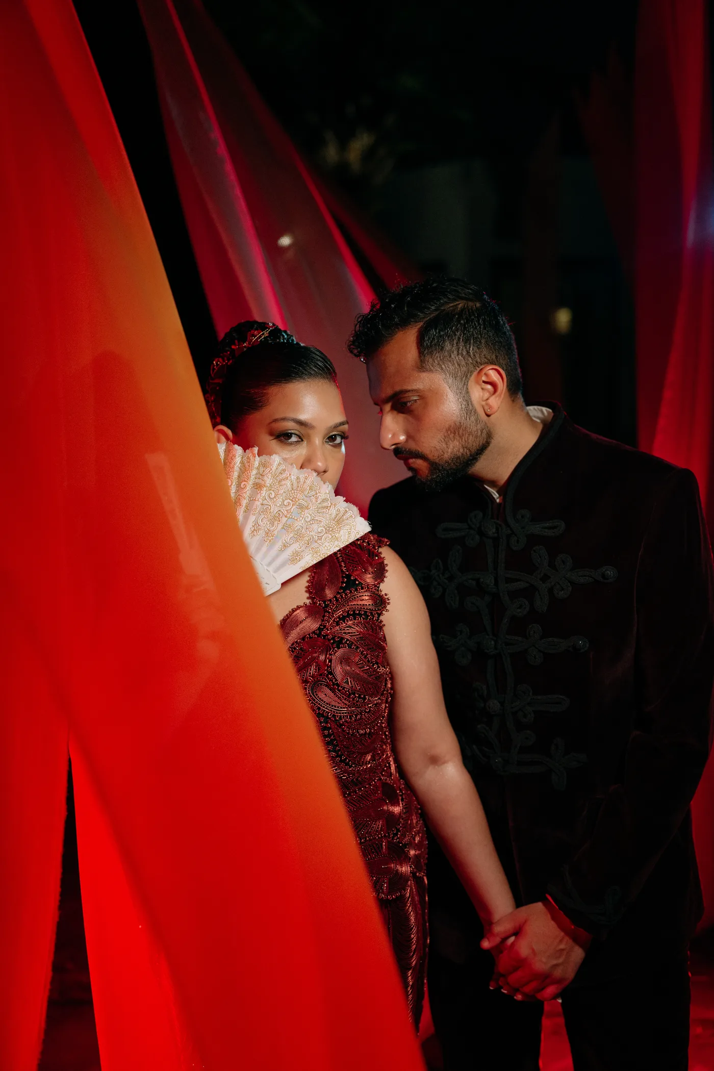An intimate moment between bride and groom behind a lace fan, lit in red